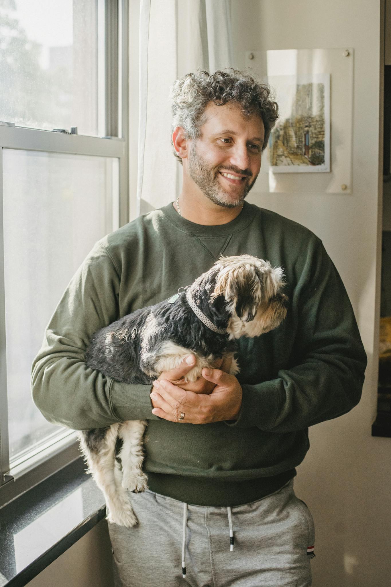A cheerful man holding his Yorkshire Terrier in a sunlit room, embodying warmth and companionship.