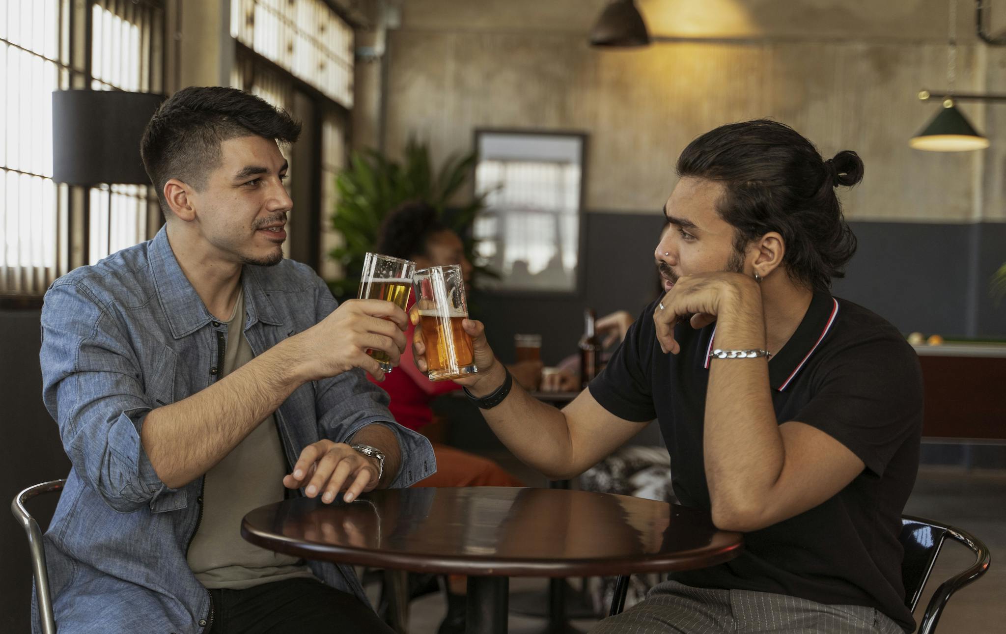 Two men enjoying a friendly conversation over beers in a cozy indoor cafe setting.