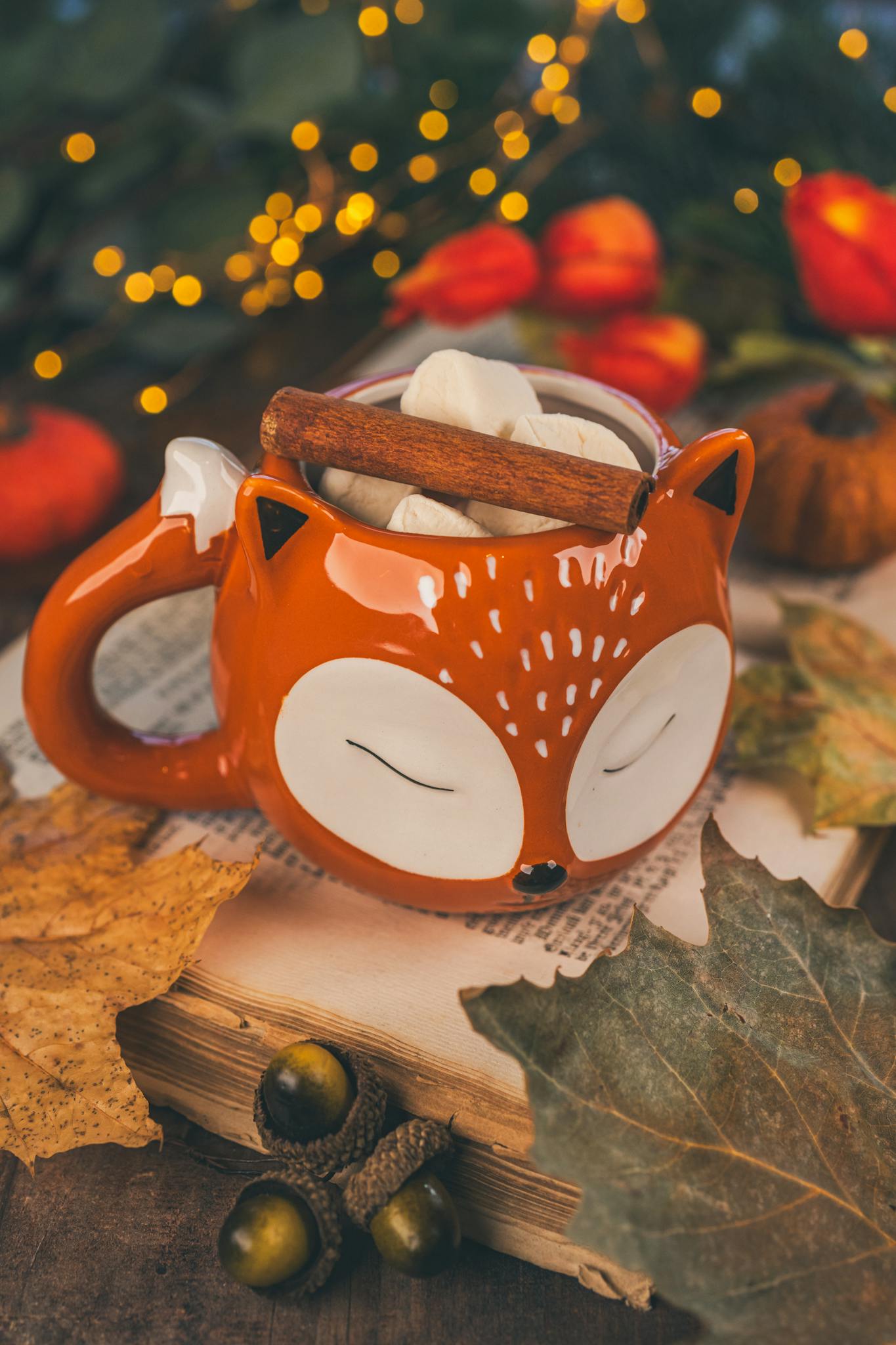 Warm autumn-themed setting with a cute animal mug filled with marshmallows and a cinnamon stick.